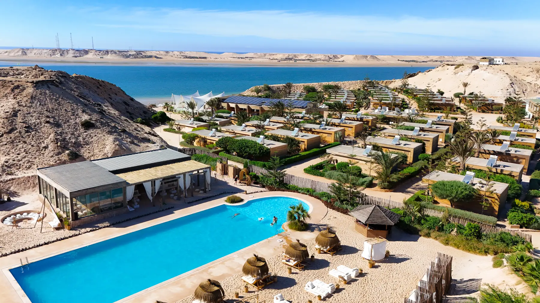 Vue aérienne du Dakhla Club : la piscine, les bungalows et la lagune de Dakhla au pied des dunes
